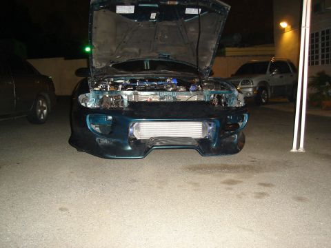 1995 Mazda MX-6 - Teal coupe with hood open, front bumper removed, revealing an aftermarket intercooler. Another vehicle is parked to the left.