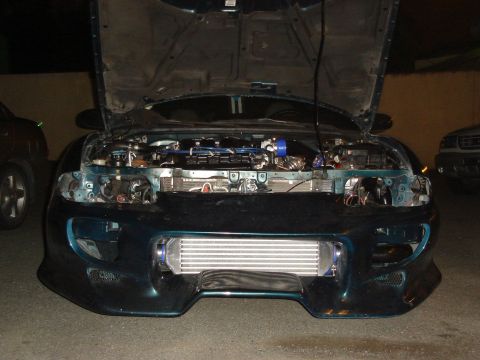 1995 Mazda MX-6 - Front view of a dark teal car with hood open, revealing engine modifications and an aftermarket intercooler. Other vehicles are partially v…
