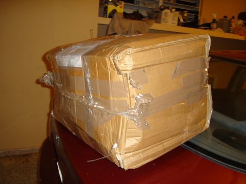 1995 Mazda MX-6 - A large, taped cardboard box sits on the trunk of a red vehicle, obscuring most of the car's details.