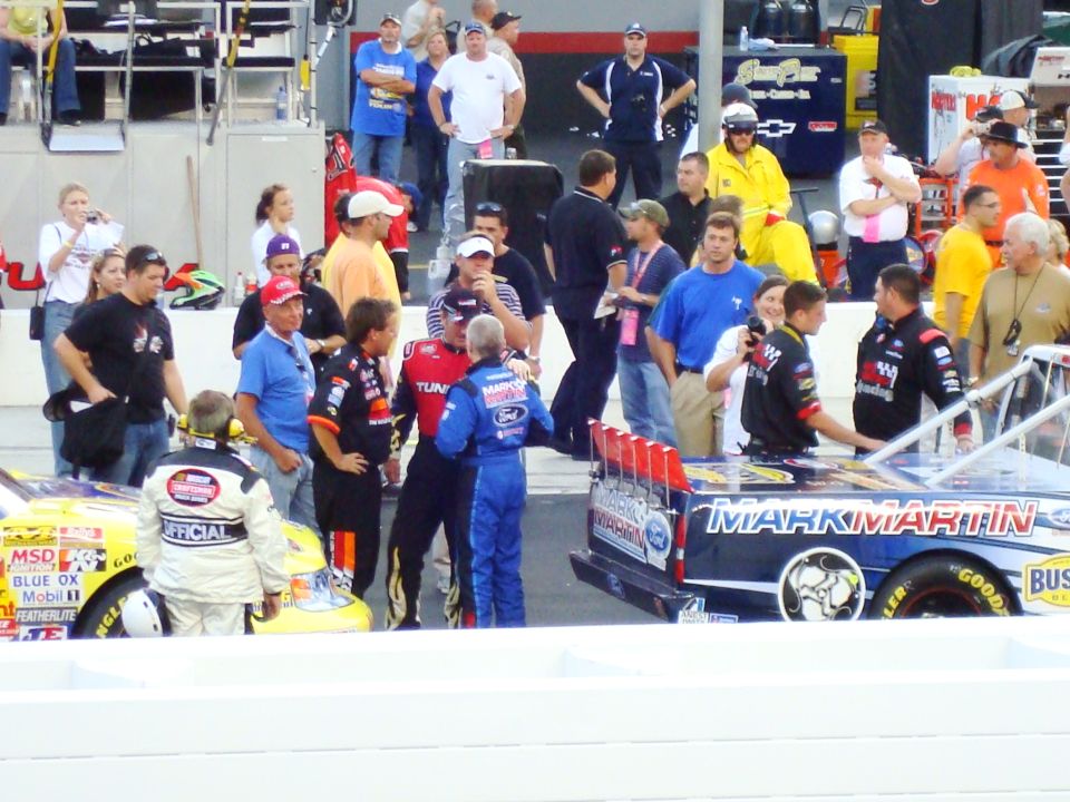 Race cars and pit crew at a NASCAR event. One car has 'MARK MARTIN' on it