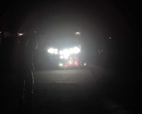 1990 Ford Bronco - A person stands in silhouette, facing a vehicle with its bright lights on at night.