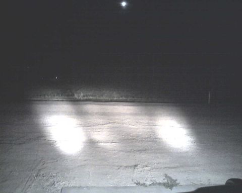 1990 Ford Bronco - Headlights shine brightly on a dark road at night, with a distant light source visible.