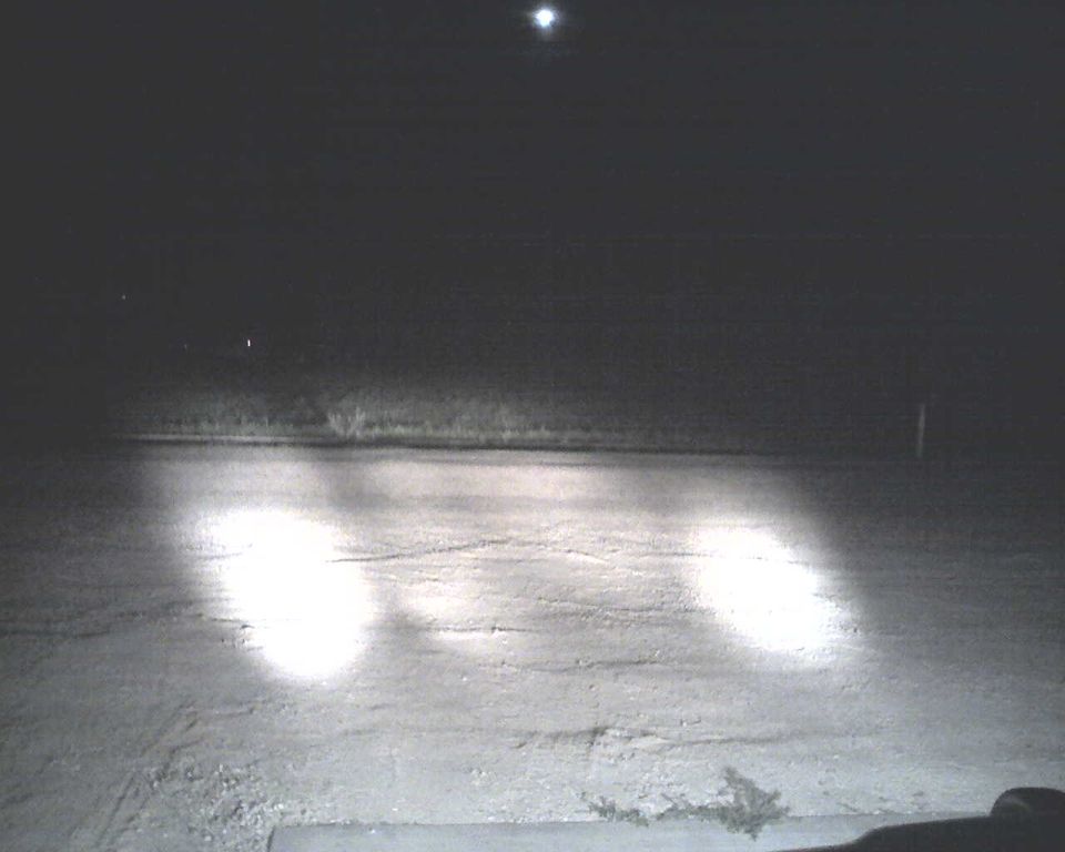 Headlights illuminate a dark, paved surface at night
