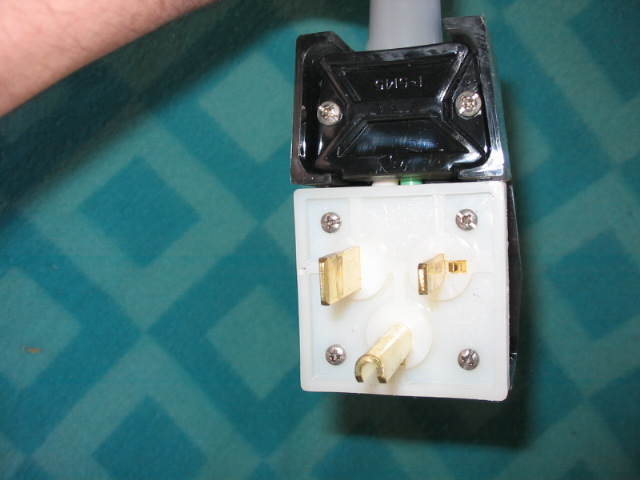 Black and white electrical plug with brass prongs on gray cord