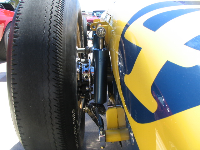 Close-up of a racing tire and yellow and blue custom bodywork with visible suspension components