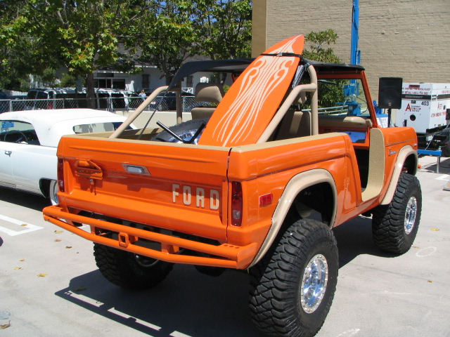 Orange Ford Bronco with a surfboard in the bed, parked next to a white convertible