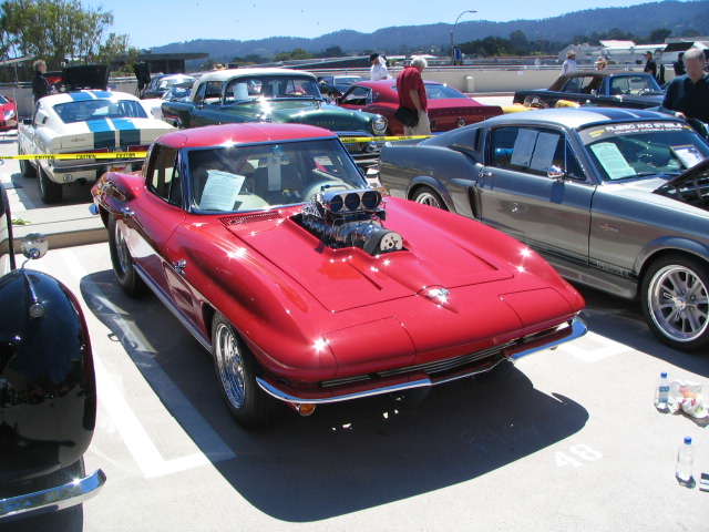 Red hot rod with a large blower on the hood, parked in a lot with other cars