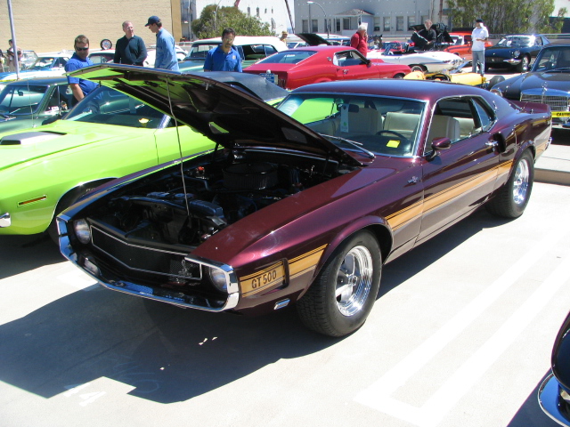 Maroon 1969 Ford Mustang GT500 with gold stripes, hood open, parked outdoors