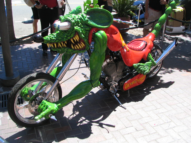 Motorcycle shaped like a green monster rat with red seat and chrome pipes
