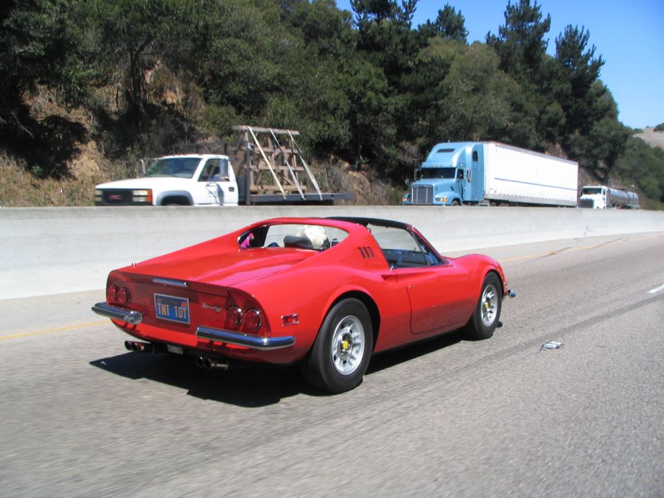 Red sports car with a license plate reading "TNT 101" driving on a highway