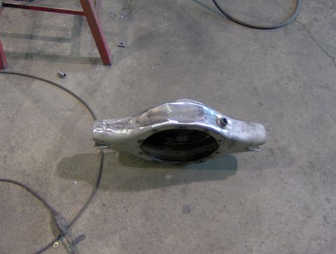 1978 Ford Bronco - A bare metal axle housing sits on a workshop floor, ready for repair or installation.