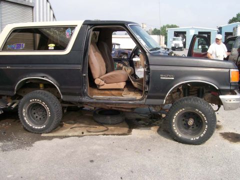 1989 Ford Bronco - 1989 Ford Bronco with doors removed and tires off, parked outdoors.