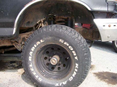 1989 Ford Bronco - The front wheel and suspension components of a vehicle are visible in this close-up shot.