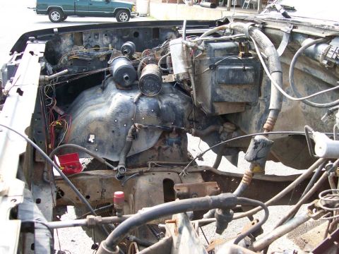 1989 Ford Bronco - The engine bay of a damaged vehicle is shown, with a green pickup truck in the background.