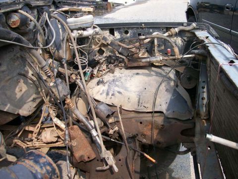 1989 Ford Bronco - The engine bay of a vehicle shows significant damage and disarray, with numerous wires and mechanical parts exposed.
