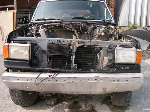 1989 Ford Bronco - The front of a 1989 Ford Bronco is shown with its hood open and grille removed, revealing the engine bay.