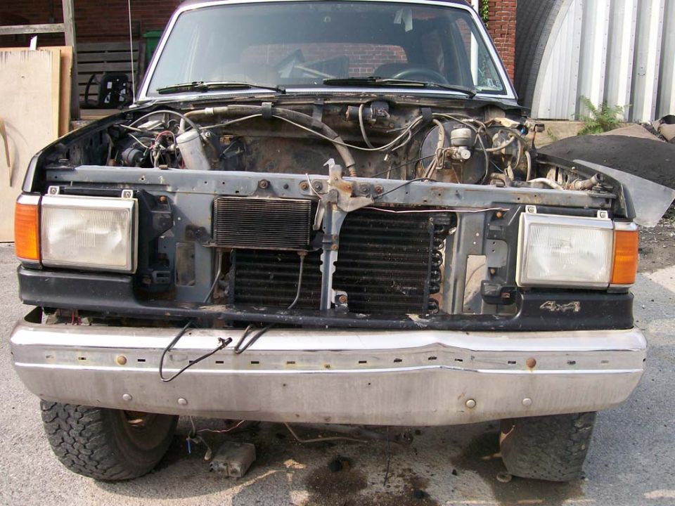 Front of a 1989 Ford Bronco with hood open and grille removed, showing engine components