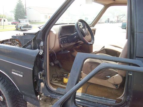1989 Ford Bronco - Interior view of a dark gray Ford Bronco, with the driver's door ajar, revealing tan upholstery and dashboard details.