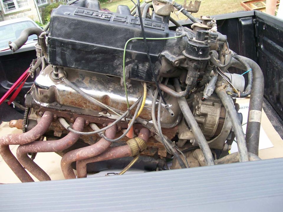 Ford V8 engine with exhaust manifolds and alternator visible, sitting in a truck bed
