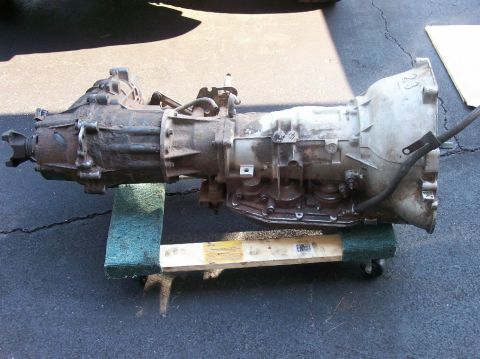 1989 Ford Bronco - A transmission assembly is shown resting on a wooden dolly with wheels. Text on the dolly indicates SUPERMOTORS.NET.