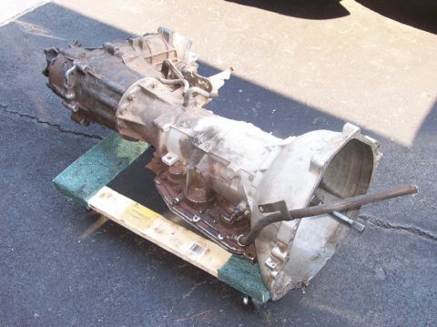 1989 Ford Bronco - Automatic transmission unit resting on wooden blocks on pavement.