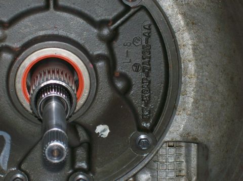 1989 Ford Bronco - Close-up of a transmission component showing a splined shaft and a red seal, with part number RF-E50AP-7A105-AA stamped on the housing.
