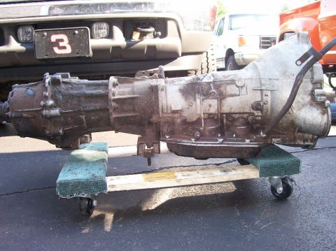 1989 Ford Bronco - An automatic transmission is shown on a wheeled dolly, with a truck's front end in the background.