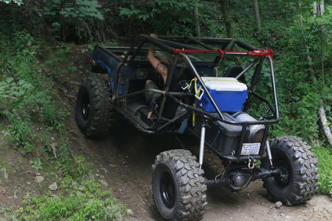 1992 Ford Mustang - This heavily modified off-road buggy, possibly a 1974 Ford Bronco, navigates a steep dirt trail with a prominent roll cage and large tires.