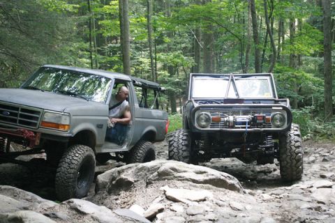 1992 Ford Mustang - Two Ford Broncos tackling a challenging off-road path in a wooded area.