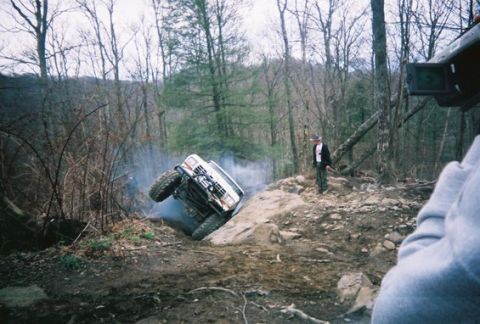 1992 Ford Mustang - An off-road vehicle navigates a challenging rocky terrain, creating smoke as it climbs.