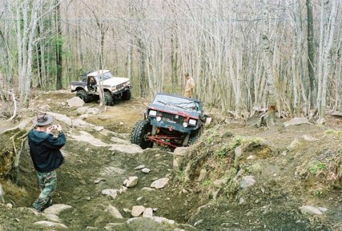 1992 Ford Mustang - Off-road vehicles tackle a challenging, rocky path in a wooded area.