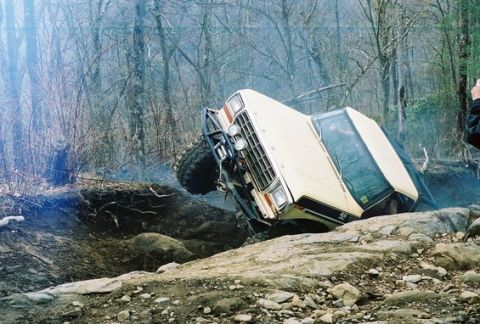 1992 Ford Mustang - An off-road vehicle navigates a difficult rocky terrain, getting stuck on its side.