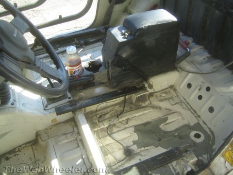 1987 Suzuki Samurai - Gutted interior of a 1987 Suzuki Samurai viewed from the driver's side, showing the black steering wheel with a Sun brand horn button, bare…