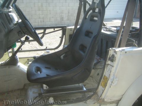 1987 Suzuki Samurai - Interior view of a stripped 1987 Suzuki Samurai showing a black fiberglass racing bucket seat mounted on a metal frame, with a tubular roll…
