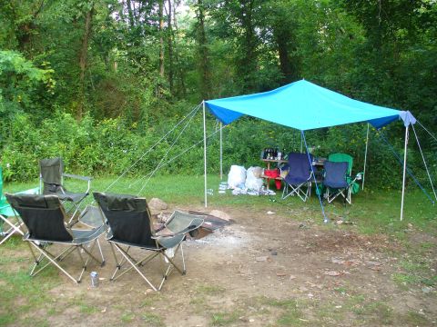 1991 Ford Probe - A campsite is set up with a blue tarp providing shade over a table and chairs, with a campfire pit nearby.