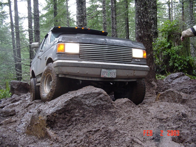 Gray Ford 4x4 climbing a muddy mound, headlights on, Oregon plate XPX-824