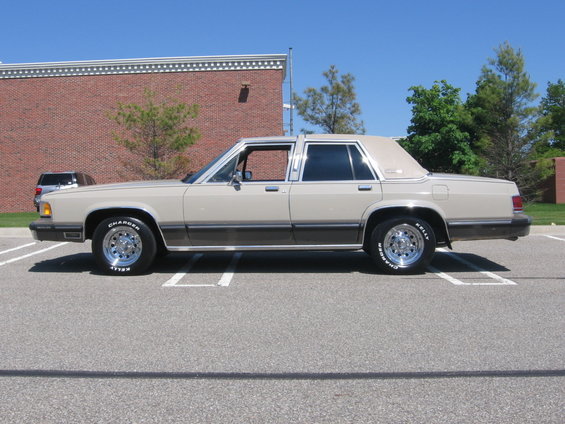 Tan full-size sedan driver-side profile beside a brick building