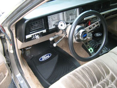 1988 Mercury Grand Marquis - The interior of a car shows Ford branded floor mats and an aftermarket steering wheel.