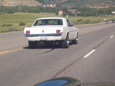 1972 Ford Ranchero - A white 1965 Ford Mustang coupe is seen driving on a highway with other vehicles in the distance.