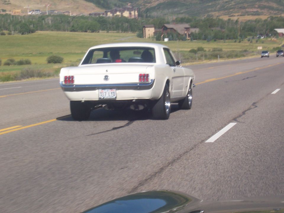 White 1965 Ford Mustang coupe rear view on highway