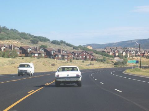 1972 Ford Ranchero - White 1967 Ford Mustang coupe on highway with a van and houses in background.