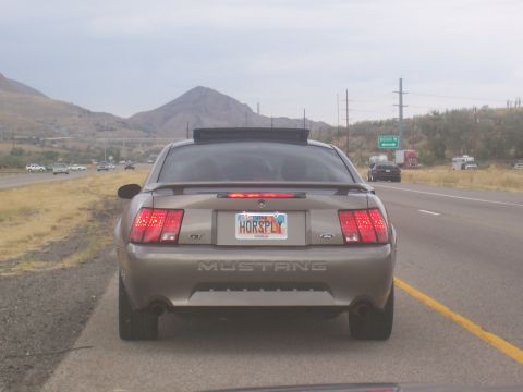 1972 Ford Ranchero - A tan Ford Mustang is seen from behind on a highway with mountains in the background.