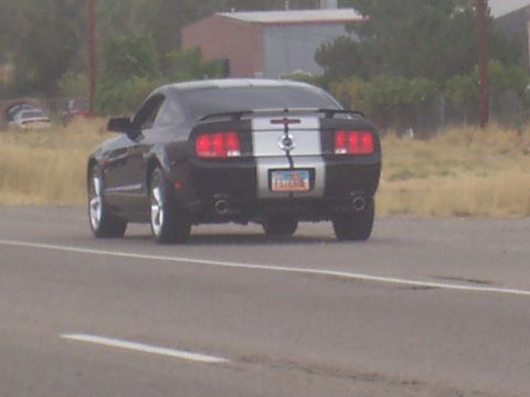 1972 Ford Ranchero - Rear view of a black coupe with silver racing stripes driving on a highway.