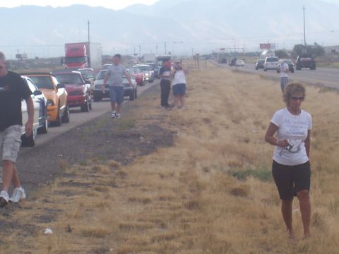1972 Ford Ranchero - A line of vehicles and people are stopped on the side of a highway with dry grass and distant mountains.