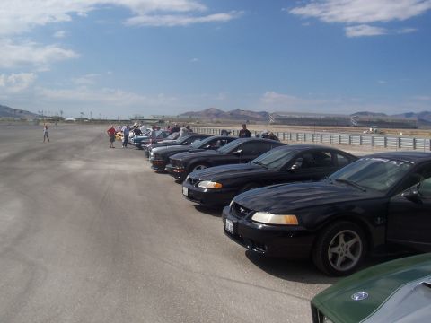 1972 Ford Ranchero - Multiple black Ford Mustangs are parked in a line on a track, with spectators and mountains visible.