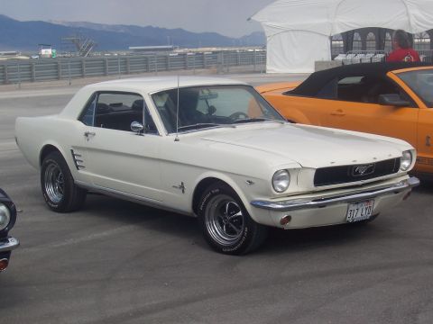 1972 Ford Ranchero - A white 1965 Ford Mustang coupe is parked next to an orange convertible, with mountains in the background.