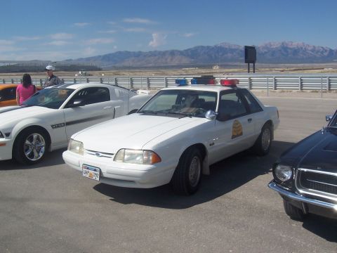 1972 Ford Ranchero - A white police car with a light bar is parked on asphalt next to other vehicles under a clear sky.
