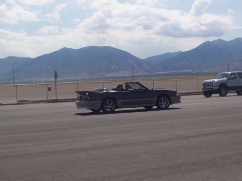 1972 Ford Ranchero - A dark convertible drives down the road with a pickup truck in the distance and mountains behind.