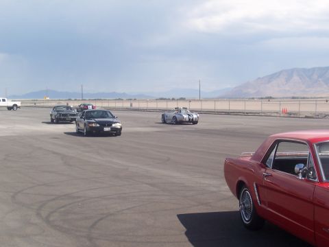 1972 Ford Ranchero - Several cars are on a paved lot with mountains in the distance under a cloudy sky.