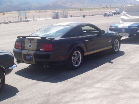1972 Ford Ranchero - A black Ford Mustang with gold racing stripes is parked at an outdoor venue next to another vehicle.
